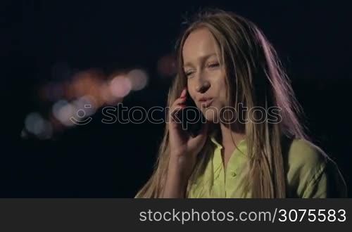 Close up view of smiling woman talking on phone over night city lights background