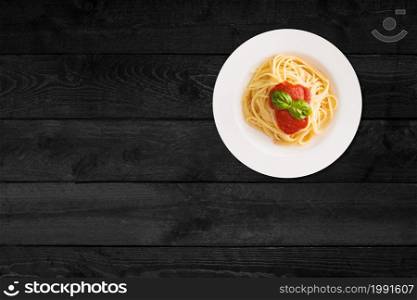 Close up view of spaghetti with ketchup isolated on black wooden table.