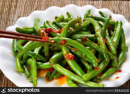 Close up view of spicy green beans with chopsticks in use. Selective focus on single bean being held by chopsticks.