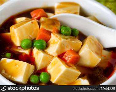 Close up view of tofu, peas, and carrots in soup with spoon in bowl.