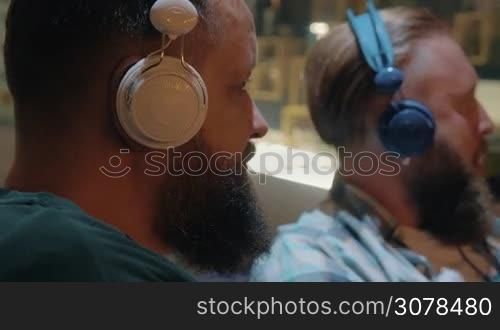 Close up view of two white mature bearded men listening musics using colorful on-ear headset