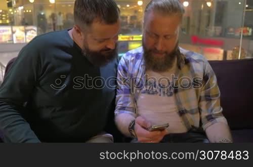 Close up view of two white mature bearded men using smartphone together. Men are relaxing and smiling