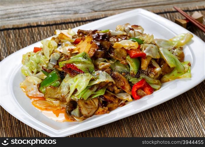 Close up view of vegetable dish consisting of eggplant, cabbage, mushrooms, and peppers in white plate with tangy sauce. Selective focus on front part of dish.