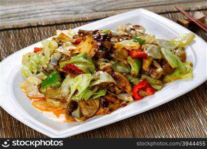 Close up view of vegetable dish consisting of eggplant, cabbage, mushrooms, and peppers in white plate with tangy sauce. Selective focus on front part of dish.
