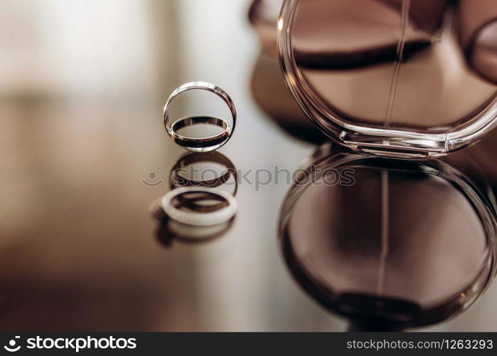 close up wedding gold rings with perfume on a glass table. wedding preparation. copy space.. close up wedding gold rings with perfume on a glass table. wedding preparation. copy space