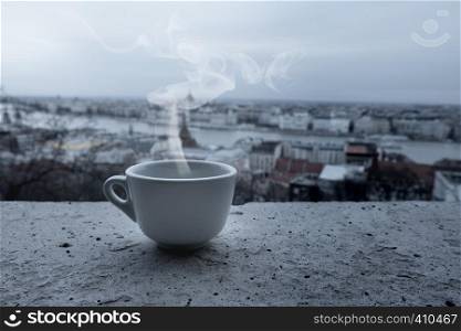 Close up white coffee cup on balcony over blurred view of city building. City skyline panorama