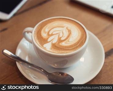 Close up white coffee cup with latte art on wood table at coffee shop