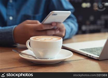 Close up white coffee cup with latte art on wood table on The background is blurred with the businessman using the phone at coffee shop