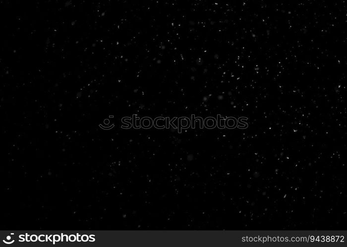 Close up white snow falling over black background of night winter sky in the dark