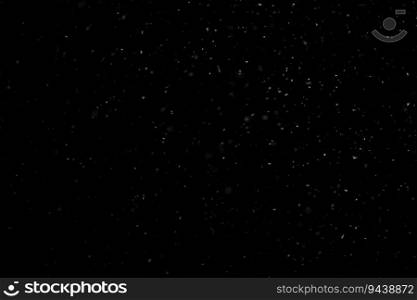 Close up white snow falling over black background of night winter sky in the dark