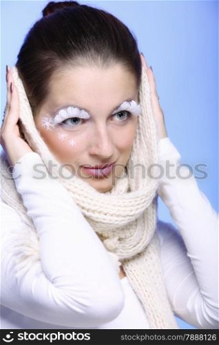 Close up winter fashion beauty woman stylish creative make up false long white eye lashes covering her ears with warm scarf blue background