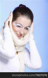 Close up winter fashion beauty woman stylish creative make up false long white eye lashes covering her ears with warm scarf blue background