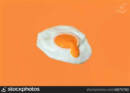 Close-up with a single sunny side up egg isolated on an orange background. Flying fried egg with the egg yolk drippin minimalist on a vibrant colored background.