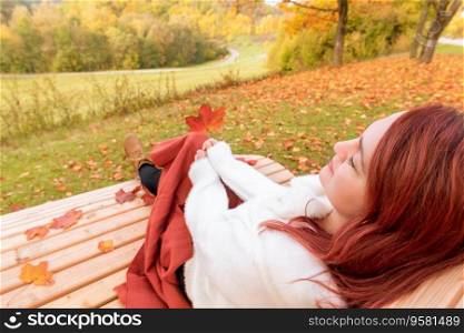 Close-up with a young woman sitting on a bench covered with an orange blanket. Woman enjoying a beautiful day of autumn in the park