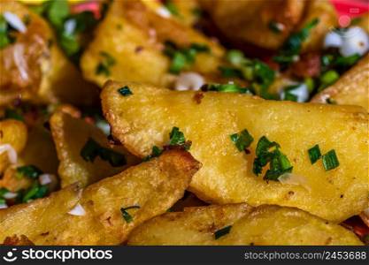 Close up with selective focus of fried potatoes with green onion, green garlic and spices in a colorful plate.