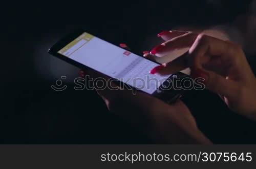 Close up woman&acute;s hand holding cellphone and texting message outdoors on blurred night lights background