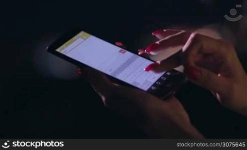 Close up woman&acute;s hand holding cellphone and texting message outdoors on blurred night lights background