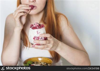 close up woman eating raspberry from yogurt