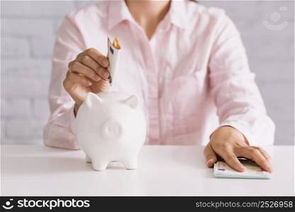 close up woman inserting euro note white piggybank