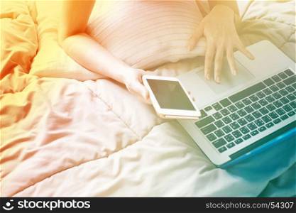 Close up Woman lying on bed with a laptop computer and smartphone on the lazy day, color transition style and gradient color