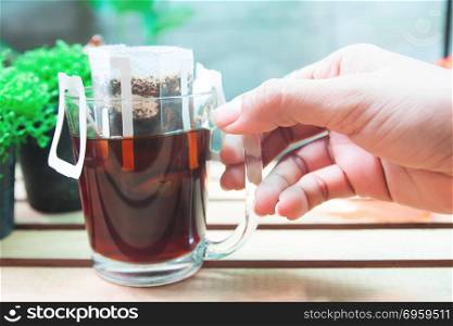 Close up woman&rsquo;s hand with a glass of drip coffee,Drip bag fresh. Close up woman&rsquo;s hand with a glass of drip coffee,Drip bag fresh coffee with garden view in background