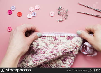 close up woman s hand measuring knitted fabric with buttons safety pins crochet needle