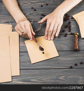 close up woman s hand pouring melt wax envelop wooden texture background