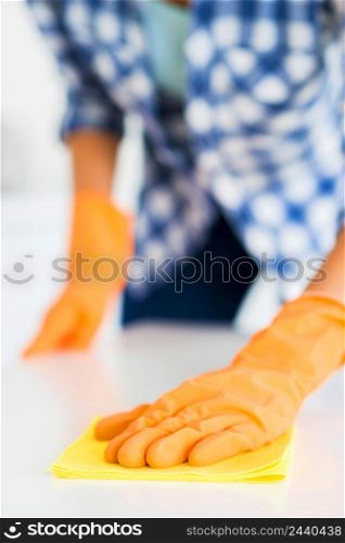 close up woman s hand wearing yellow gloves wipes white surface with yellow napkin