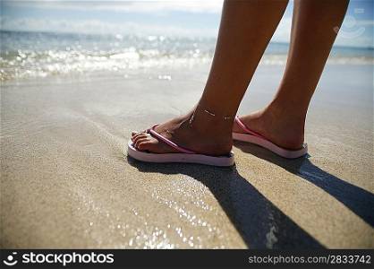 Close-up woman standing on a beach wearing flip-flops