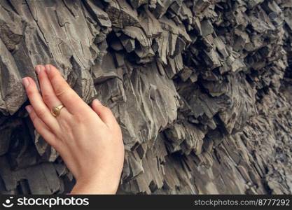 Close up woman touching basalt rock concept photo. Black stone. First view hand photography with textured stone on background. High quality picture for wallpaper, travel blog, magazine, article. Close up woman touching basalt rock concept photo