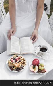 close up woman turning pages book with breakfast coffee table
