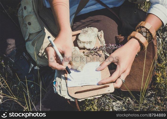 Close up woman writing notes during hike concept photo. Top view person photography with green meadow on background. High quality picture for wallpaper, travel blog, magazine, article. Close up woman writing notes during hike concept photo