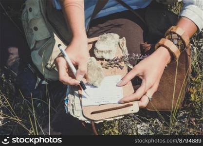 Close up woman writing notes during hike concept photo. Top view person photography with green meadow on background. High quality picture for wallpaper, travel blog, magazine, article. Close up woman writing notes during hike concept photo