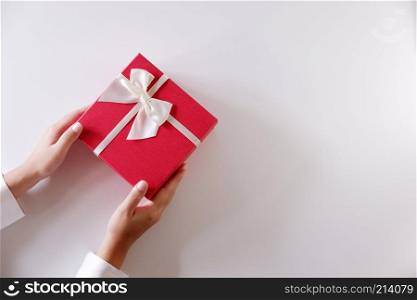 Close-up women hands sending red gift box with white ribbon on white background