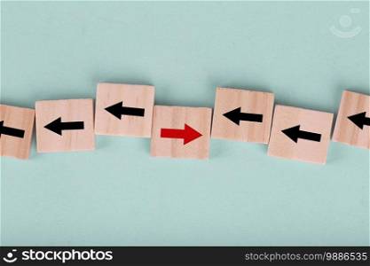 Close up wooden block on blue background with red arrow facing the opposite direction black arrows , Concept of think differently and individual