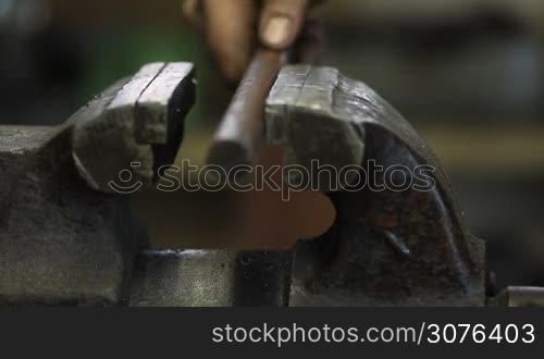 Close up worker fixing steel shaft with bench vise tool in workshop