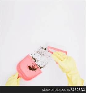close up yellow gloved hands sweeping dust into dustpan white background