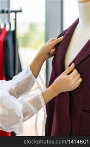 Close-up young adult asian fashion designer checking at suit arm on mannequin at her atelier studio as before deliver to her customer. For entrepreneur small business startup work from home concept.