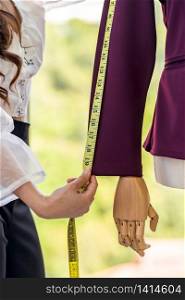 Close-up young adult asian fashion designer using measuring tape to measure suit arm at her atelier studio as sole owner. Using for entrepreneur small business startup concept.