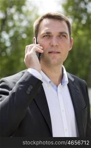 Close up, young businessman calling by phone in summer street