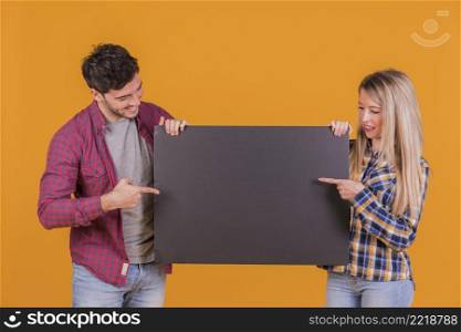 close up young couple pointing their fingers black placard against orange background