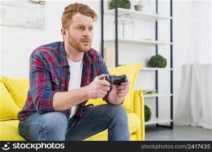 close up young man sitting yellow sofa playing video game with joystick living room