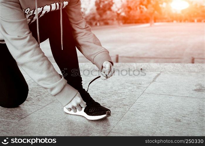 close up young woman tying shoelace while walking, sunny day in winter season- B&W filter