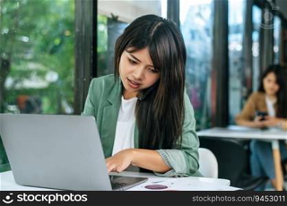 Close up, Young woman working on laptop computer, she talking with smartphone while typing and looking on paper work or report in coffee shop