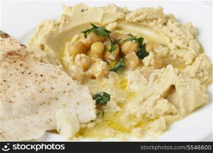 close view of Arab masbacha, hummus served with whole chickpeas and a chilli and lemon flavoured sauce. The bread in the foreground is being used to scoop it up.