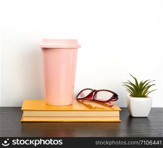 closed book and pink ceramic glass with coffee on a black table, white wall