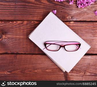 closed book with a gray cover and glasses on top