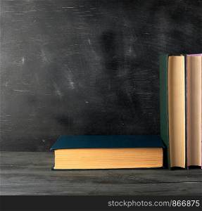 closed books with yellow sheets on a black chalk board background, copy space, back to school concept