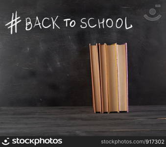 closed books with yellow sheets on a black chalk board background, hashtag back to school