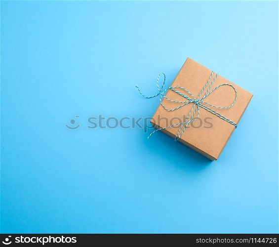 closed brown square box with a gift tied rope on a blue background, top view, empty place for an inscription